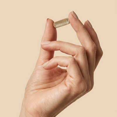 Hand holding a The Shift herbal perimenopause herbal capsule against cream background